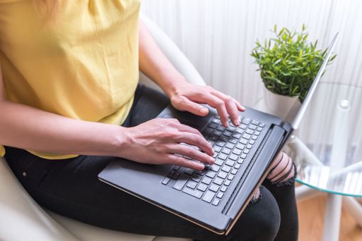 A woman sitting on a chair using a laptop on her lap