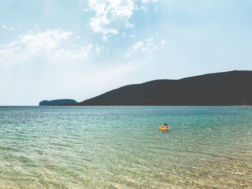 A beautiful shot of a person on the surface of the sea surrounded by high mountains under the cloudy sky