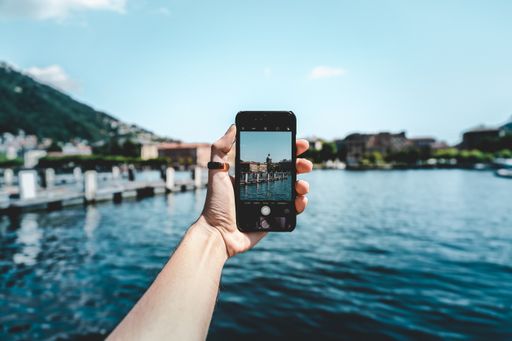 A person with a smartphone taking a picture of the beautiful view with mountains near the clear lake