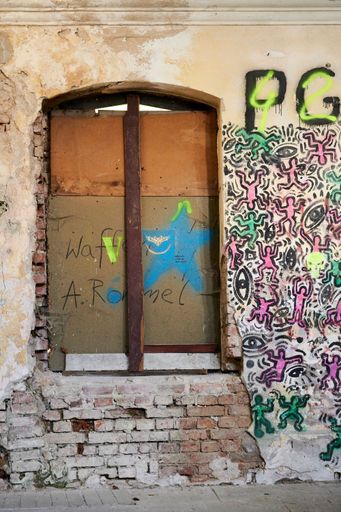 A vertical shot of a locked door and a wall with graffiti on a abandoned psychiatric building