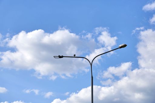 A view of a street lamp with two sides bent in opposite directions on the background of cloudy sky