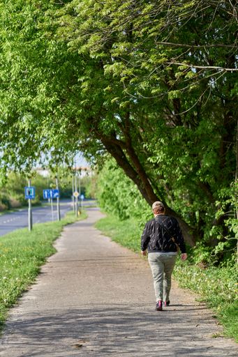 A vertical shot of a woman walking on a footpath with trees around on the Inflancka street in Warszawa, Poland