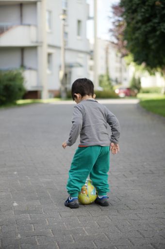 Three years old child playing with a ball on a street in the city