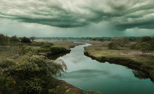 A cloudy sky over a calm river with partial vegetation on both banks