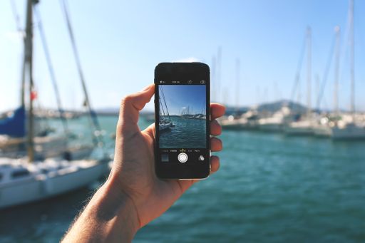 A person with a smartphone taking a picture of boats in the sea with the beautiful sky in the background