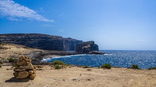 An aerial view of sea surrounded by rocky and sandy beach under blue bright sky