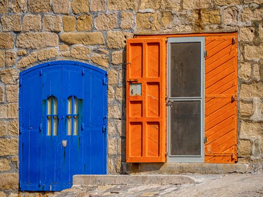 A closeup of blue door and orange window on stony building in Malta