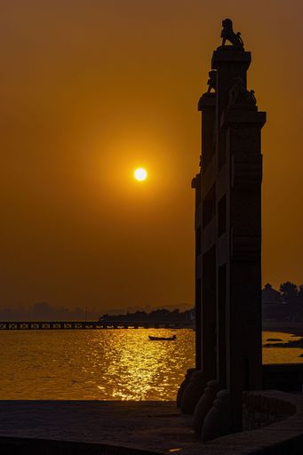 A vertical shot of a statue near the shore on the background of the beautiful sunset