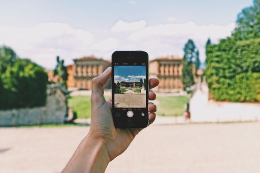 A person with a smartphone taking a picture of the beautiful view with high buildings surrounded by green trees