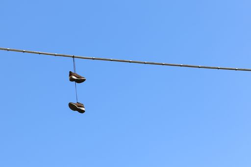 A low angle shot of a pair of shoes hanging from a cable with the breathtaking blue sky in the background