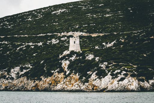 A white concrete building isolated on a green mountain near the sea during daytime