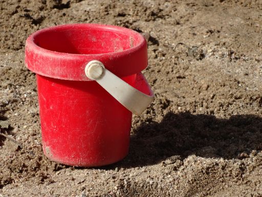 A closeup of an old red bucket on the sand under the sunlight