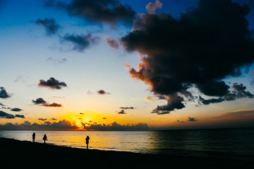 A beautiful silhouette of people walking on the seashore under the breathtaking cloudy sky during sunset