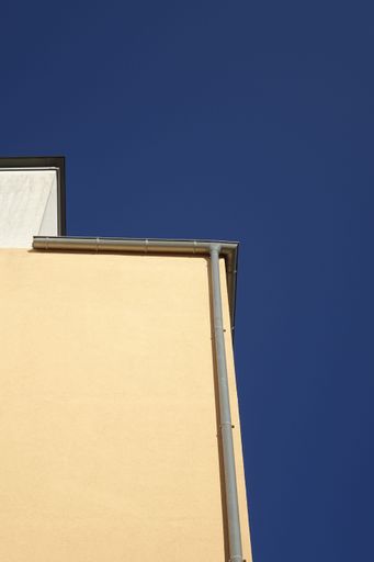 A low angle shot of beige stone building with vertical water pipe against blue sky