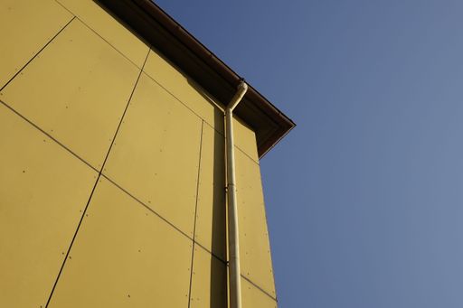 A low angle shot of yellow stone building with vertical water pipe against blue sky