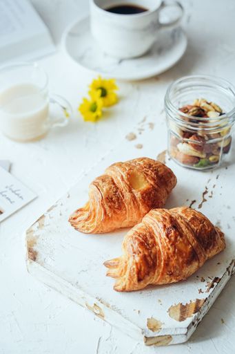 A vertical shot of two croissants, coffee, and milk on a cafe table