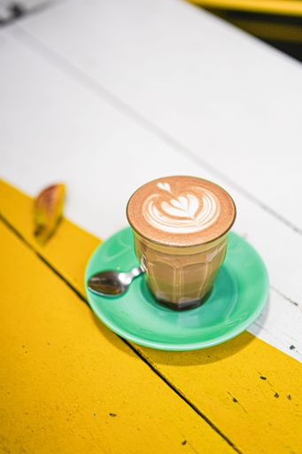 A vertical shot of a latte with foam art on a green saucer
