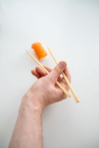 A man's hand with sticks and a piece of sushi, Salmon roll with rice on white background