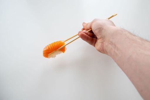 A man's hand with sticks holding a piece of sushi, Salmon roll with rice on white background