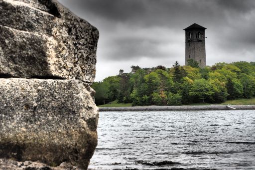 A wide-angle shot of a lighthouse in the forest near the sea during a cloudy day