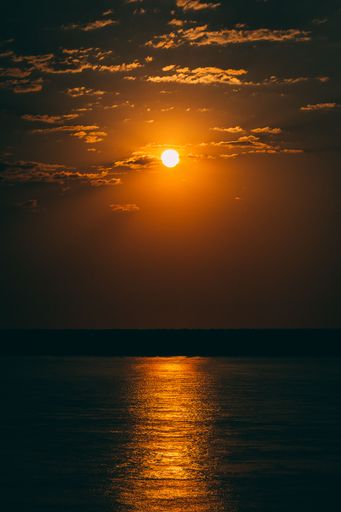A vertical breathtaking view of the golden full moon shining behind the clouds reflected in the water