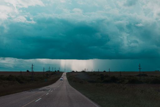 A breathtaking view of vehicles on an asphalt road cutting through green fields on blue cloudy sky background