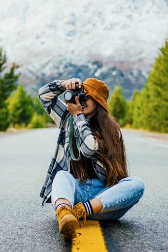 A vertical breathtaking view of a young attractive female photographer taking pictures while sitting on an asphalt road