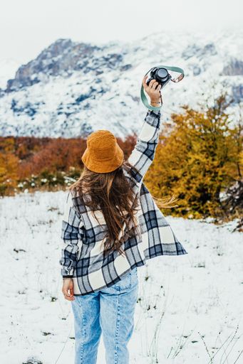 A vertical back view of a young female photographer holding her camera up in the snowy field