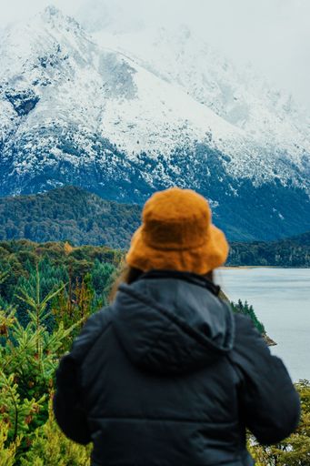 A vertical back view of a young female admiring the beauty of the frozen lake surrounded by green plants and snowy mountains