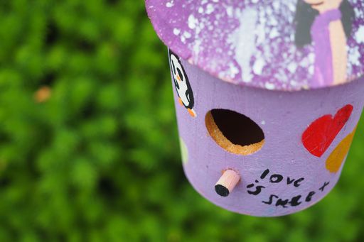A soft focus of a purple, wooden birdhouse against blurry greenery