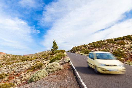 A car driving fast on El Teide road in a rural area in cloudy sky background