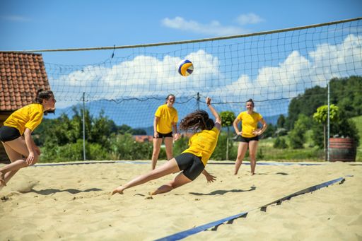 Young, hot girls in yellow t-shirts play volleyball on sand pitch on sunny summer day