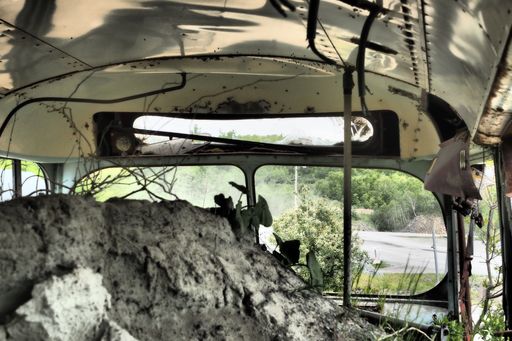 An inside view of an old abandoned wrecked bus in a field full of rubbish