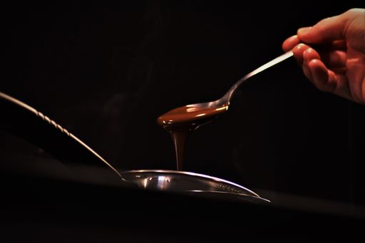 A closeup of a person picking hot melted chocolate with a spoon on a dark background
