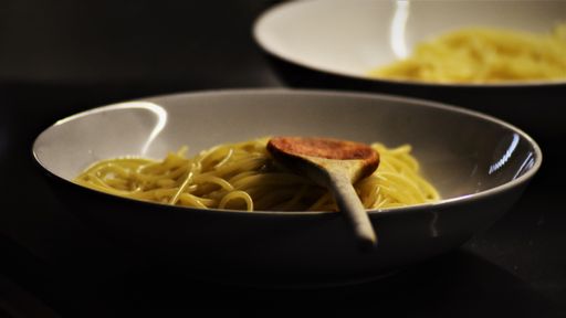 A closeup of cooked pasta in a bowl with a wooden spoon on the table