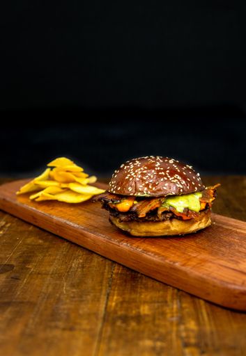 A vertical shot of cheeseburger sandwich with fried potatoes chips on wood isolated on black background