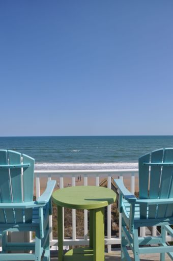 A vertical shot of two blue chairs and a green table overlooking the ocean