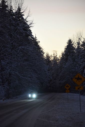 A vertical shot of a car on a snowy road during sunset
