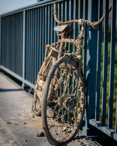 An old rusty bicycle parked in the street next to metal fences