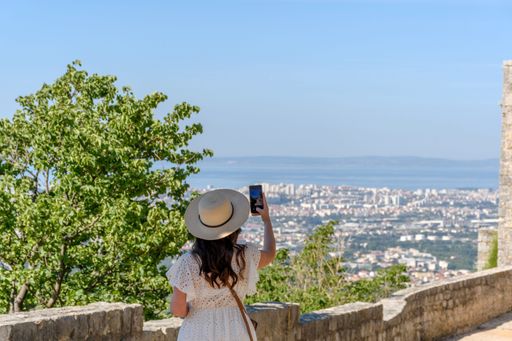 A Caucasian woman standing at Klis fortress, taking photos of coastal city of Split, Croatia