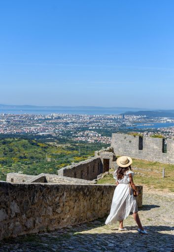 A Caucasian woman standing at Klis fortress, taking photos of coastal city of Split, Croatia
