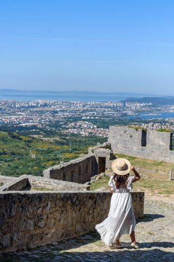 A caucasian young woman in white dress at Klis fortress overlooking coastal city of Split in Croatia