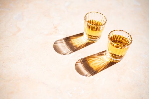 A high angle shot of small crystal glasses with white wine reflected on the ground