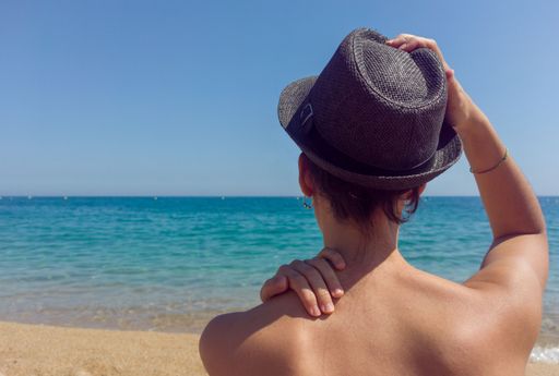 A close-up from the back of a woman looking at the sea with a black hat