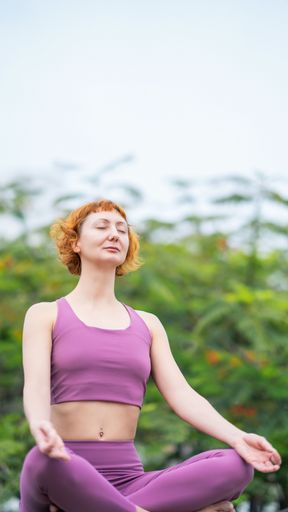 A Caucasian woman yogini meditating on a natural organic tree background with a clear sky
