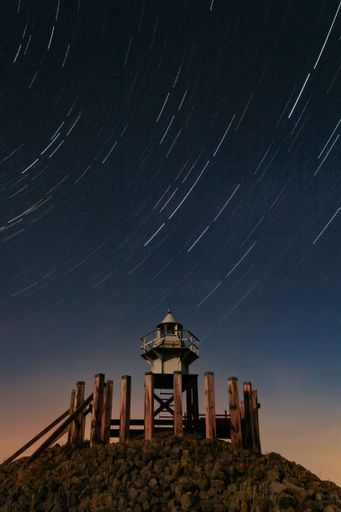 A vertical shot of a Star trails over a beacon surrounded by wood at night