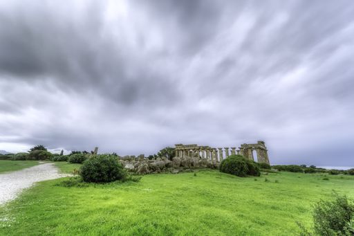 A wide shot of isolated abandoned building ruins in a green field under the dark cloudy sky