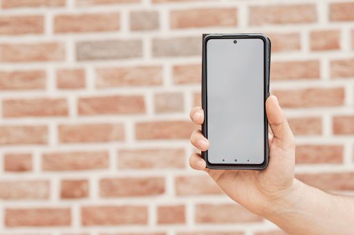 A hand holding a smartphone with white screen on the background of brick wall