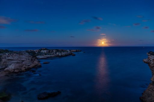 A horizontal shot of the blue sea surrounded by cliffs during the sunset