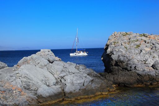 A beautiful shot of the rocks near a body of water with a white yacht sailing in the distance. Almunecar, Spain